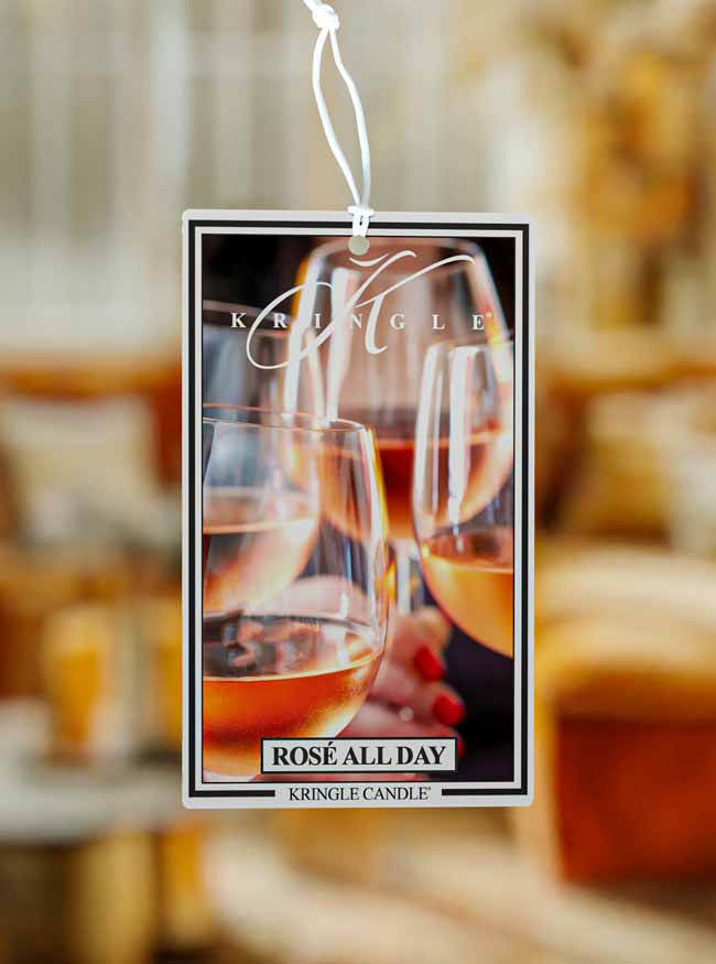 Kringle Candle Rose All Day hanging scent card air freshener with blurred wine glasses in the background