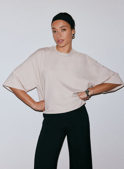 Model wearing a sand-colored Luxe Boxy Short Sleeve top and black pants, hands on hips [M-170cm]