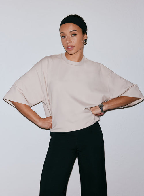 Model wearing a sand-colored Luxe Boxy Short Sleeve top and black pants, hands on hips [M-170cm]