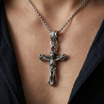 Close-up of a sterling silver skeleton crucifix pendant featuring a red gemstone accent, worn on a silver chain by a model in a dark shirt, showcasing intricate gothic biker style jewelry.