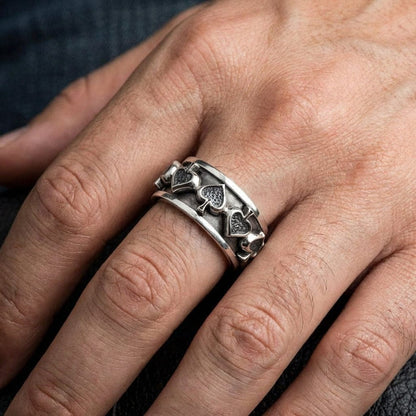 Sterling silver spade spinner ring featuring playing card suit symbols worn on a man's ring finger, showcasing the wide band design with oxidized finish and raised spade motifs in a lifestyle product shot