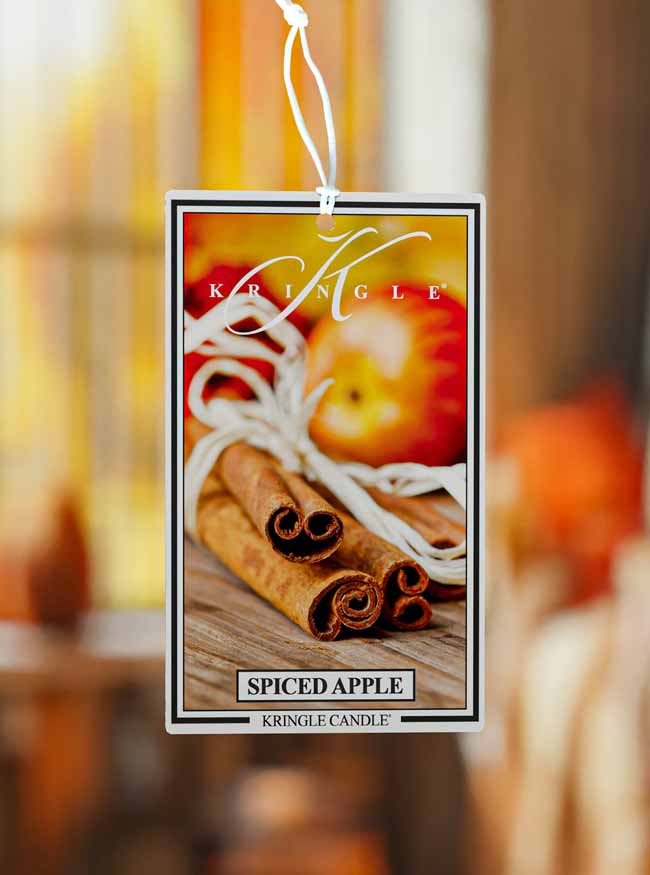 Kringle Candle Spiced Apple air freshener with cinnamon sticks and apples on a blurred background