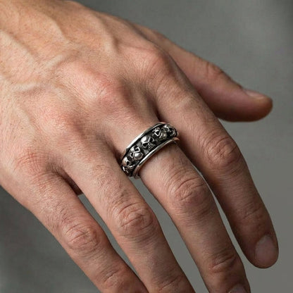 Sterling silver skull spinner ring with oxidized finish worn on a man's finger, featuring multiple skull motifs around the band in a gothic biker style