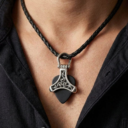 Silver tribal guitar pick holder pendant with ornate Celtic-style scrollwork design holding a black guitar pick, worn on a braided black leather cord necklace against a man's chest with open black shirt