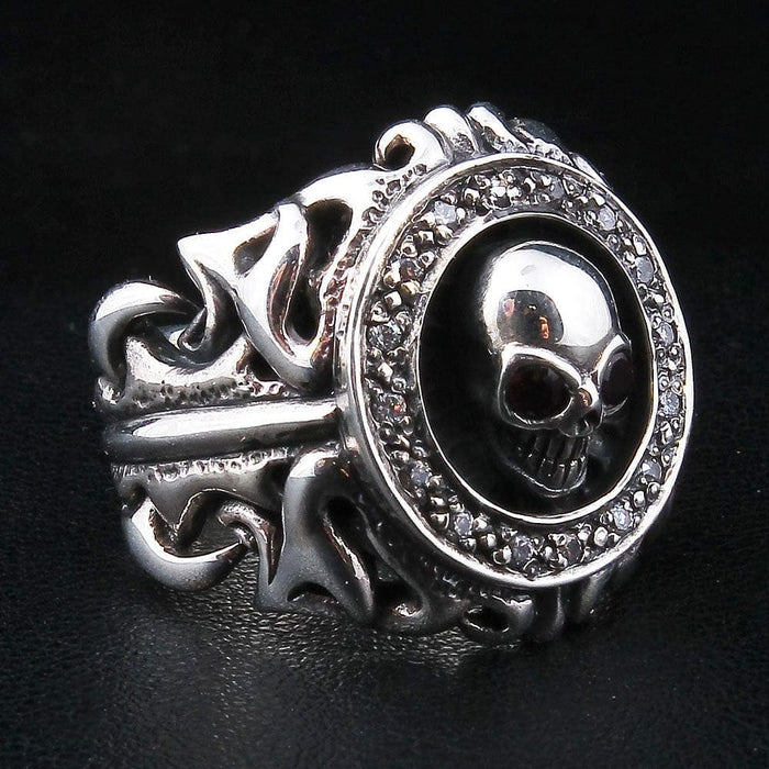 Tribal garnet skull silver ring at a three-quarter angle, skull ringed by a clear CZ halo over an openwork scroll band.