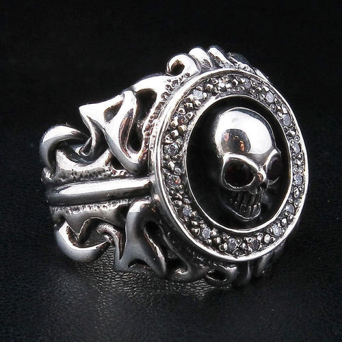 Tribal garnet skull silver ring at a three-quarter angle, skull ringed by a clear CZ halo over an openwork scroll band.