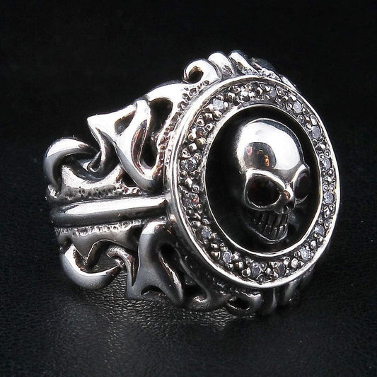 Tribal garnet skull silver ring at a three-quarter angle, skull ringed by a clear CZ halo over an openwork scroll band.
