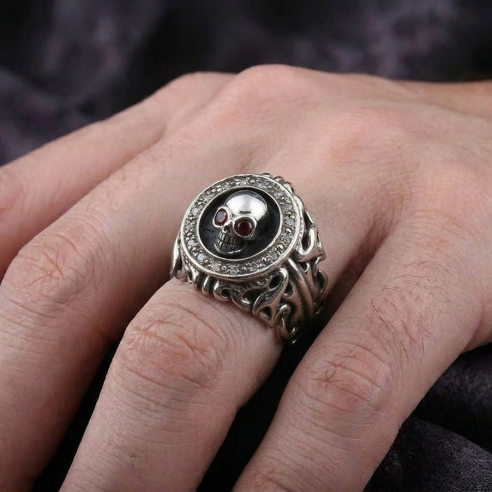 Close-up of a sterling silver gothic skull ring with red garnet eyes worn on a man's hand.