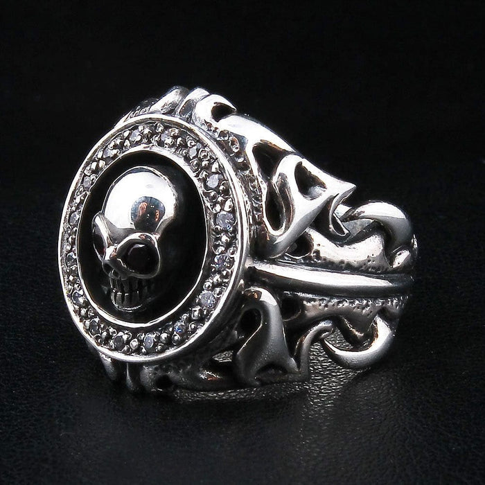 Angled view of the garnet skull ring from the right, the CZ halo and skull set above deep openwork tribal scrollwork.