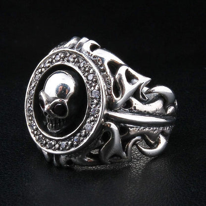 Angled view of the garnet skull ring from the right, the CZ halo and skull set above deep openwork tribal scrollwork.