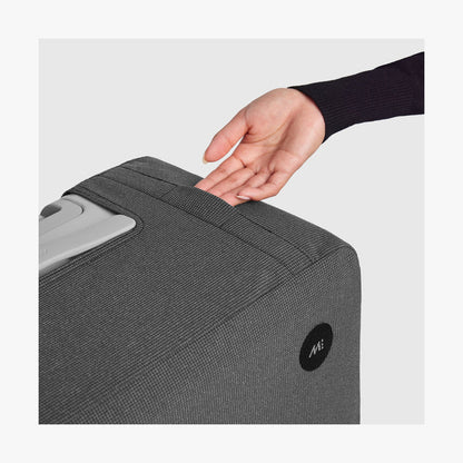 Carry-On | Hand placed under the top grab handle pocket of the grey Monos Washable Luggage Cover over a suitcase