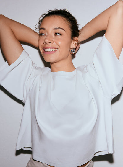 Smiling model wearing a white Luxe Boxy Short Sleeve top, with hands behind head [M-170CM]