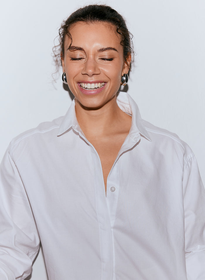 A smiling woman wearing a white oxford shirt with her eyes closed and curly hair. [M-170cm]