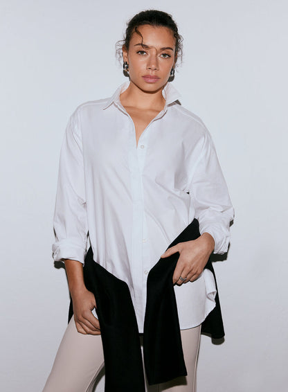 A woman wearing a white long-sleeve oxford shirt, light pants, and a black garment over her arm, looking at the camera. [M-170cm]