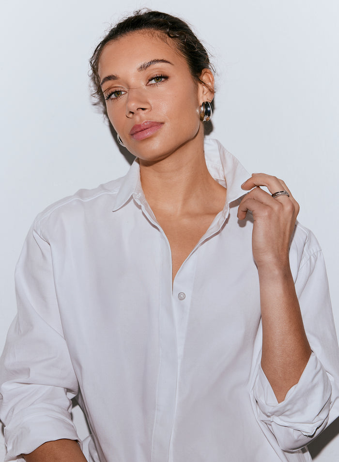 A woman wearing a white Oxford shirt, looking at the camera and holding her collar. [M-170CM]